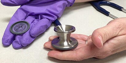 Hands holding a 3M™ Littmann® Classic III™ Stethoscope chestpiece.
